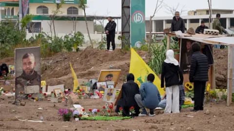 Lebanese gather next to graves at a cemetery in southern Lebanon, where Hezbollah flags and photos of Hezbollah fighters are on display
