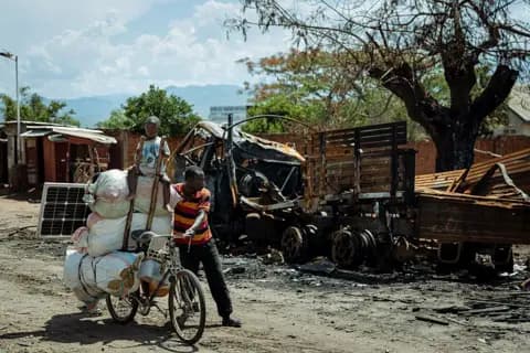  A displaced man accompanied by his child, returns from Kigubhe where he had sought refuge, as he passes a charred military vehichle in Luvungi on December 13, 2025